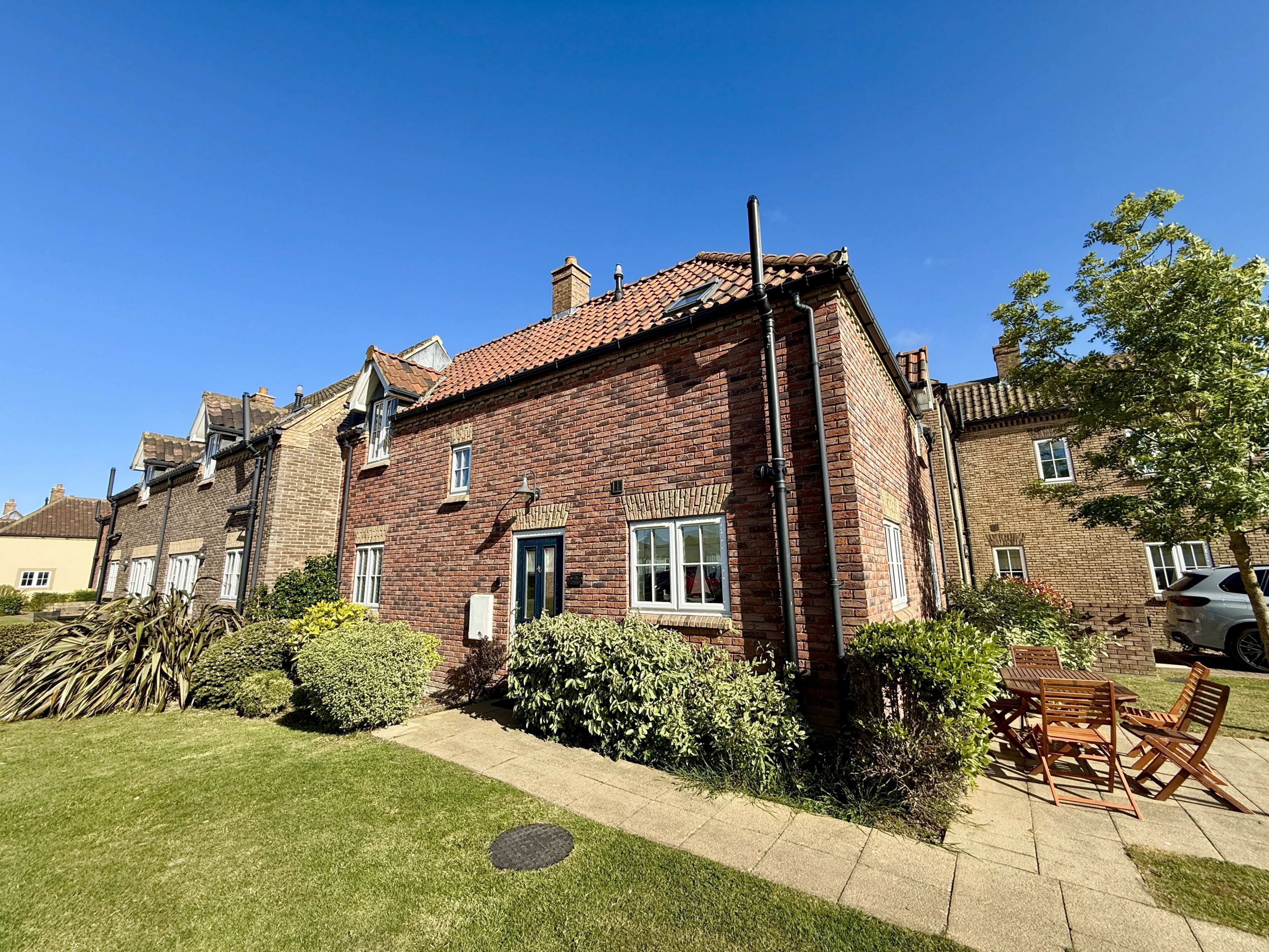 A brick house with a tiled roof, a front door, and a small front yard with a lawn and bushes.