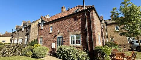 A brick house with a tiled roof, a front door, and a small front yard with a lawn and bushes.
