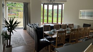 Zona pranzo con tavolo apparecchiato per quattro, divano e vista su un paesaggio verde attraverso ampie finestre.