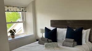 Un letto rifatto con lenzuola bianche, due cuscini blu scuro e una coperta a righe.