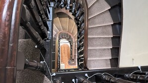 Una scala in legno con corrimano e vista su una stanza al piano superiore.
