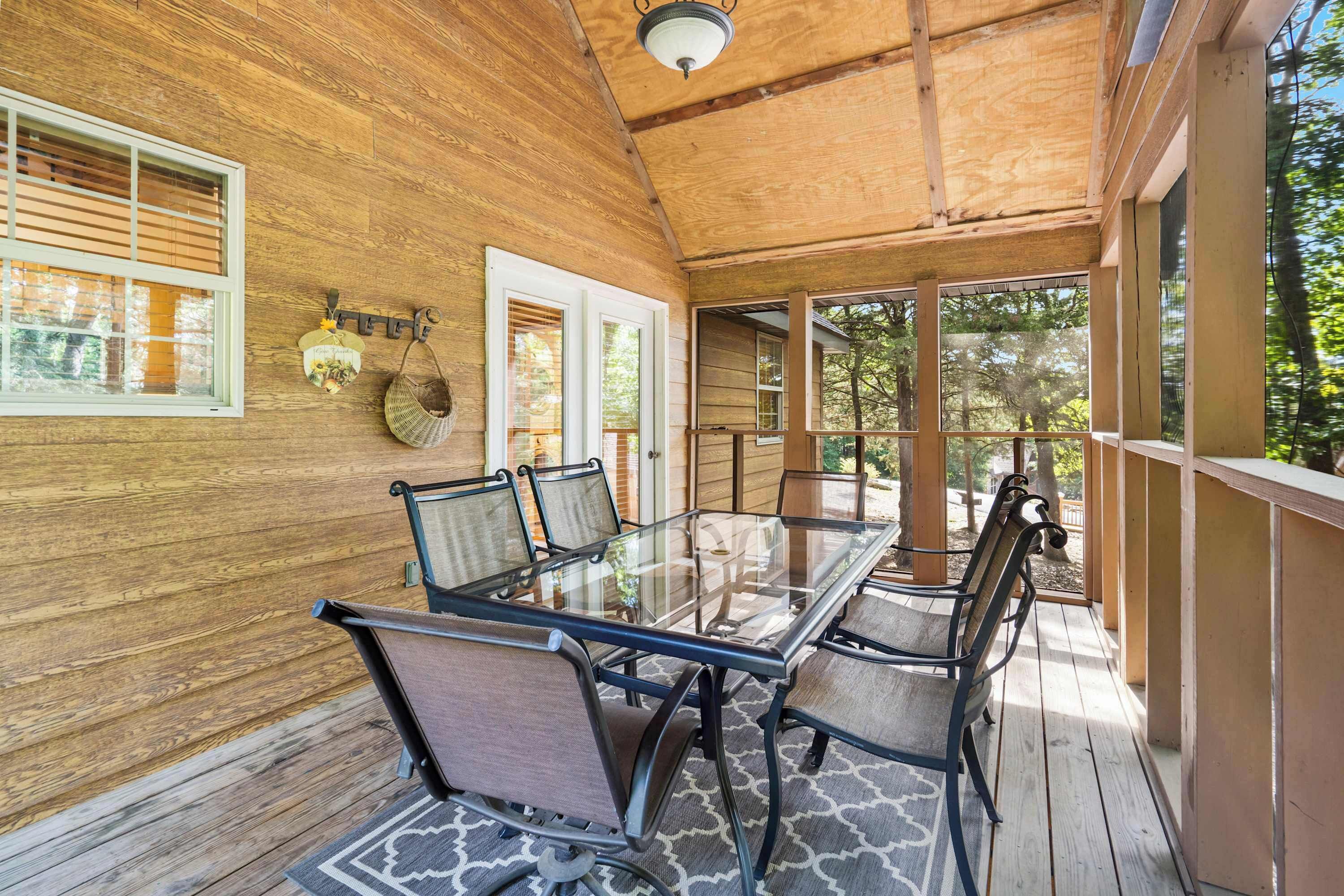 Una terraza de madera con una mesa y sillas de superficie de vidrio, rodeada de paredes y puertas de madera.