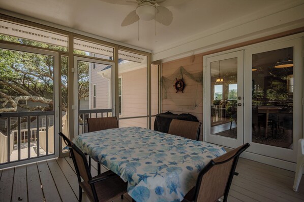 Une terrasse couverte avec une table et des chaises, de grandes fenêtres et un ventilateur de plafond.