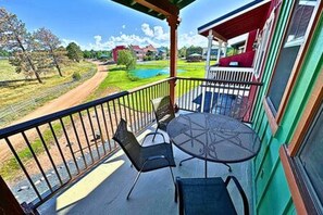 En balkon med bord og stole, der ud til et grønt landskab og et vandareal.