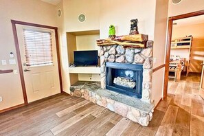 A room with a stone fireplace, a television on a stand, and a door with a window.