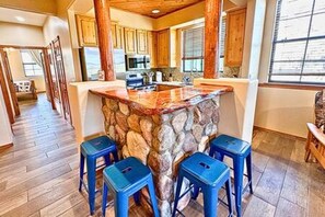 A kitchen with a stone island, wooden cabinets, and blue bar stools.