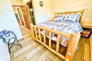 A bedroom with a wooden bed frame, a patterned bedspread, and a small folding chair.