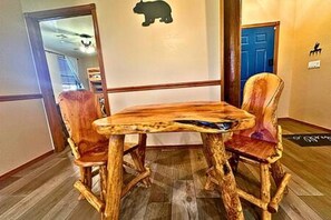 A wooden dining table with two chairs, a blue door, and a bear symbol on the wall.