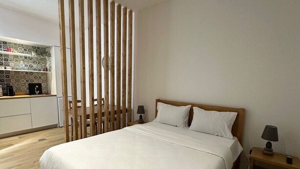 Un dormitorio moderno con estructura de cama de madera, ropa de cama blanca y una mesita de noche con lámpara.