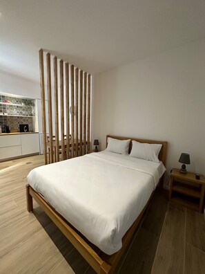 Un dormitorio moderno con estructura de cama de madera, ropa de cama blanca y una mesita de noche con lámpara.