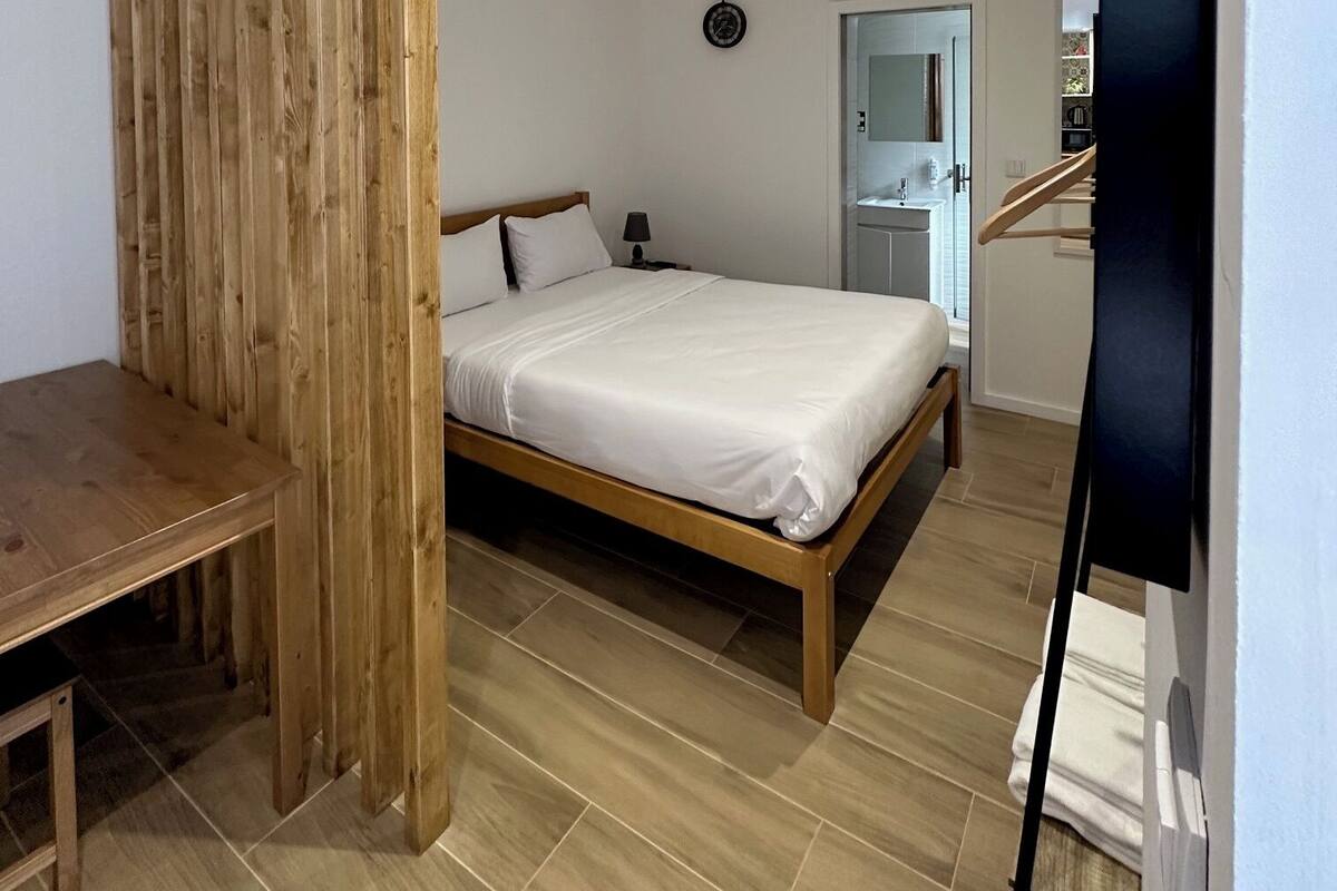 Een slaapkamer met een houten bedframe, een nachtkastje, een klein nachtkastje en een wandklok.