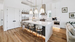 A modern kitchen with white cabinetry, a central island with bar stools, pendant lighting, and stainless steel appliances. - Relax in Style Steps to the Beach • Heated Pool, Gulf Views, & Room for Everyone (Inlet Beach)