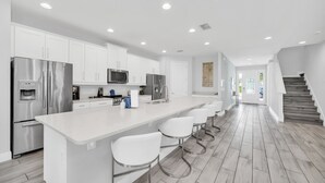A modern kitchen with white cabinets, stainless steel appliances, and a central island with bar stools.