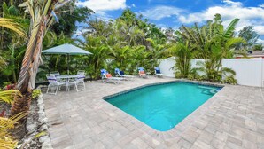 A rectangular swimming pool with a tiled deck, surrounded by lush tropical plants and a white fence. - Family Home with Private Pool, 3 mins from Beach! - Ariel's by the Sea (Holmes Beach)