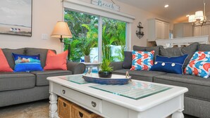 A living room with two grey sofas, colorful pillows, a white coffee table, a lamp, and a window with a view of greenery. - Family Home with Private Pool, 3 mins from Beach! - Ariel's by the Sea (Holmes Beach)
