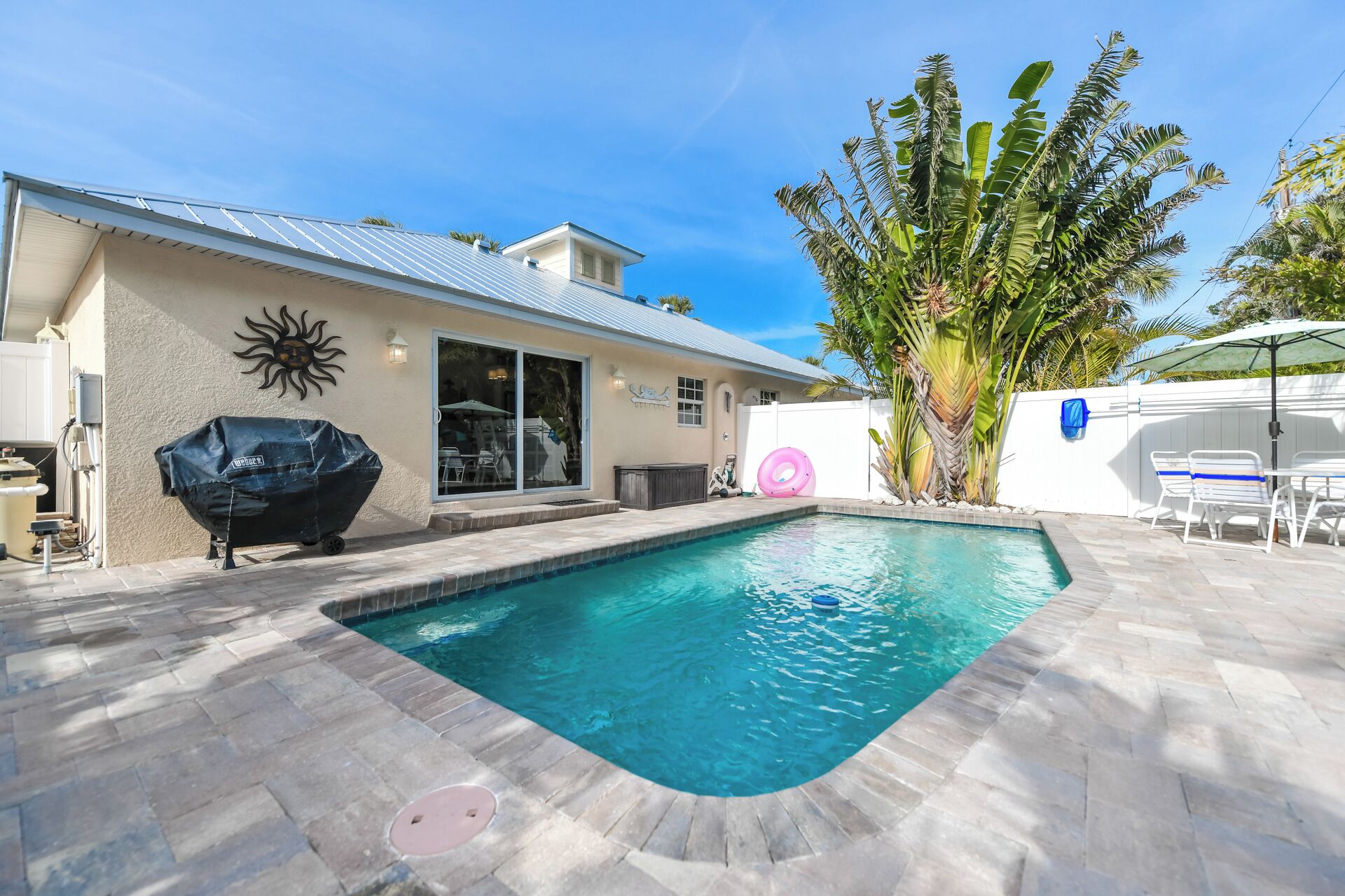A swimming pool with a stone deck, a barbecue grill, and a covered patio area.