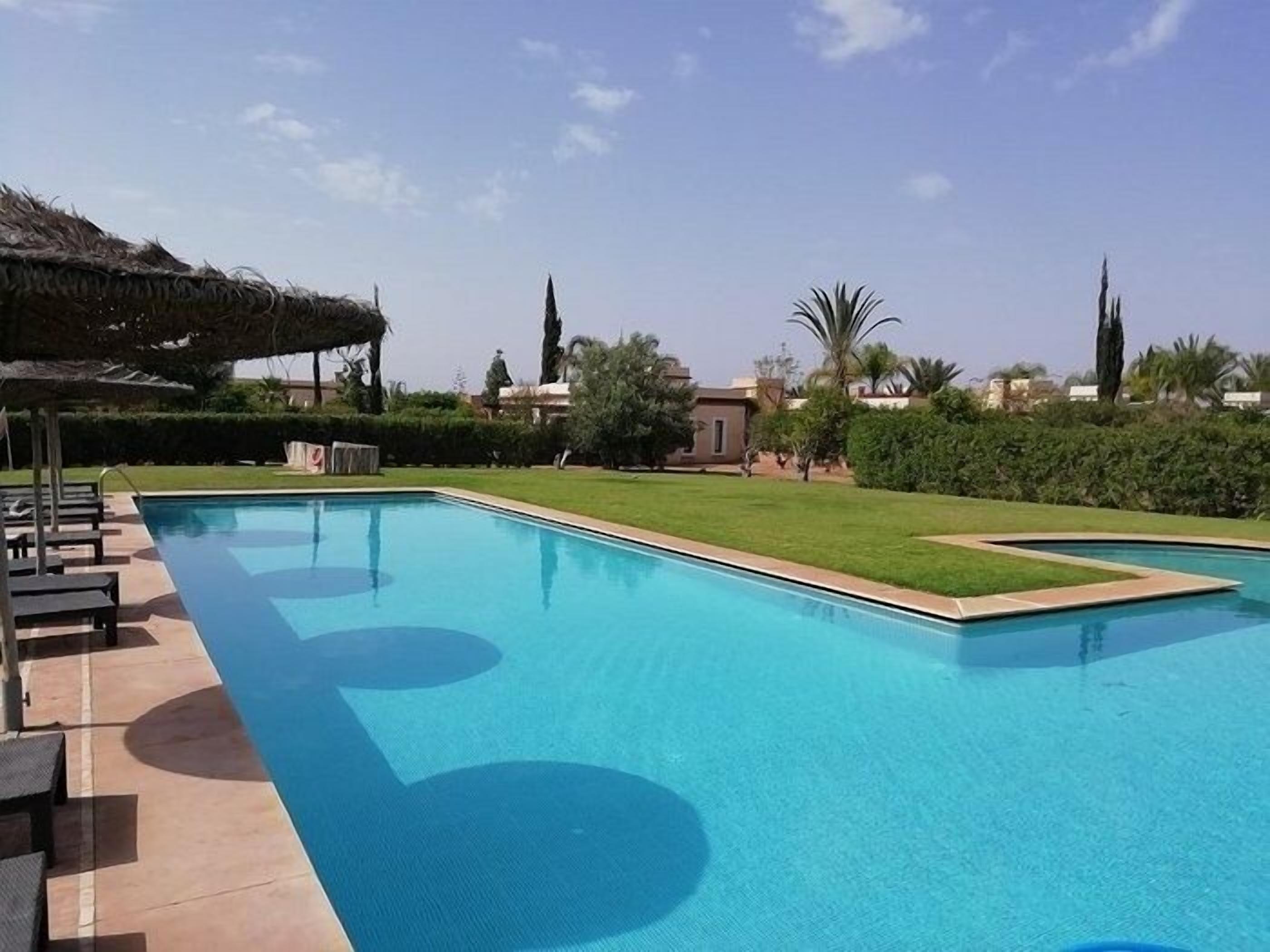 A rectangular swimming pool with a clear blue water surface, surrounded by a well-maintained lawn and a few trees.