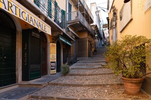 A narrow cobblestone street with buildings on either side, including a visible sign for 'Artigianale' and 'Sandwich - Mini Market'. - Stairway Apartment by Wonderful Italy (Bellagio)