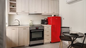 Una cocina compacta con armarios de madera clara, un horno negro, un refrigerador rojo y un pequeño comedor con una silla y una mesa negros.