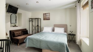 Un dormitorio con cama, sofá, una mesita y televisor montado en la pared.