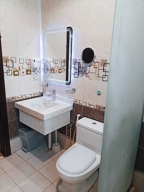 A bathroom with a white sink, mirror, and toilet. There are patterned tiles on the walls and a towel rack. - The residence hotel (Jeddah)