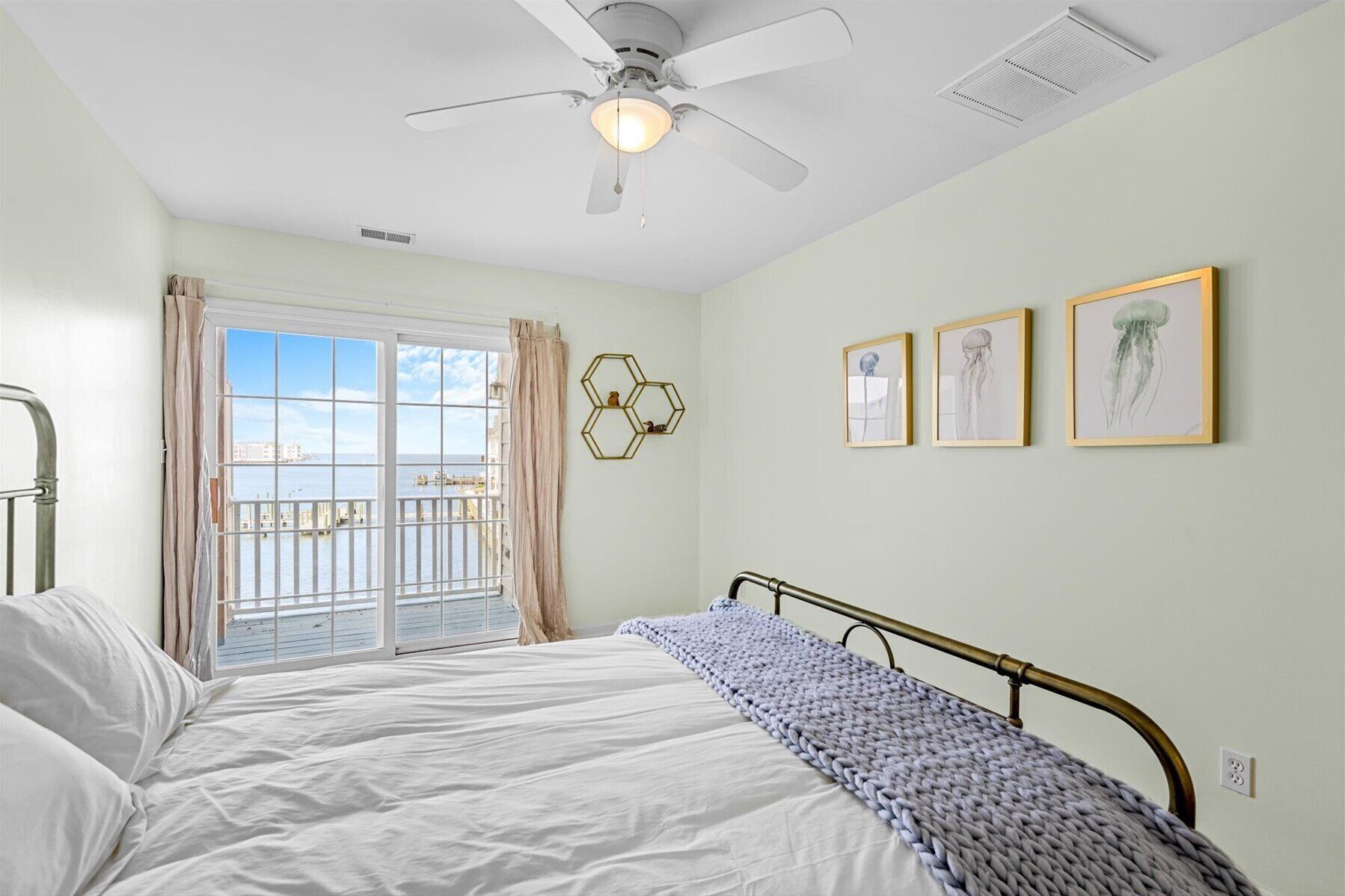 A bedroom with a bed, a ceiling fan, a window with curtains, and three framed pictures on the wall.