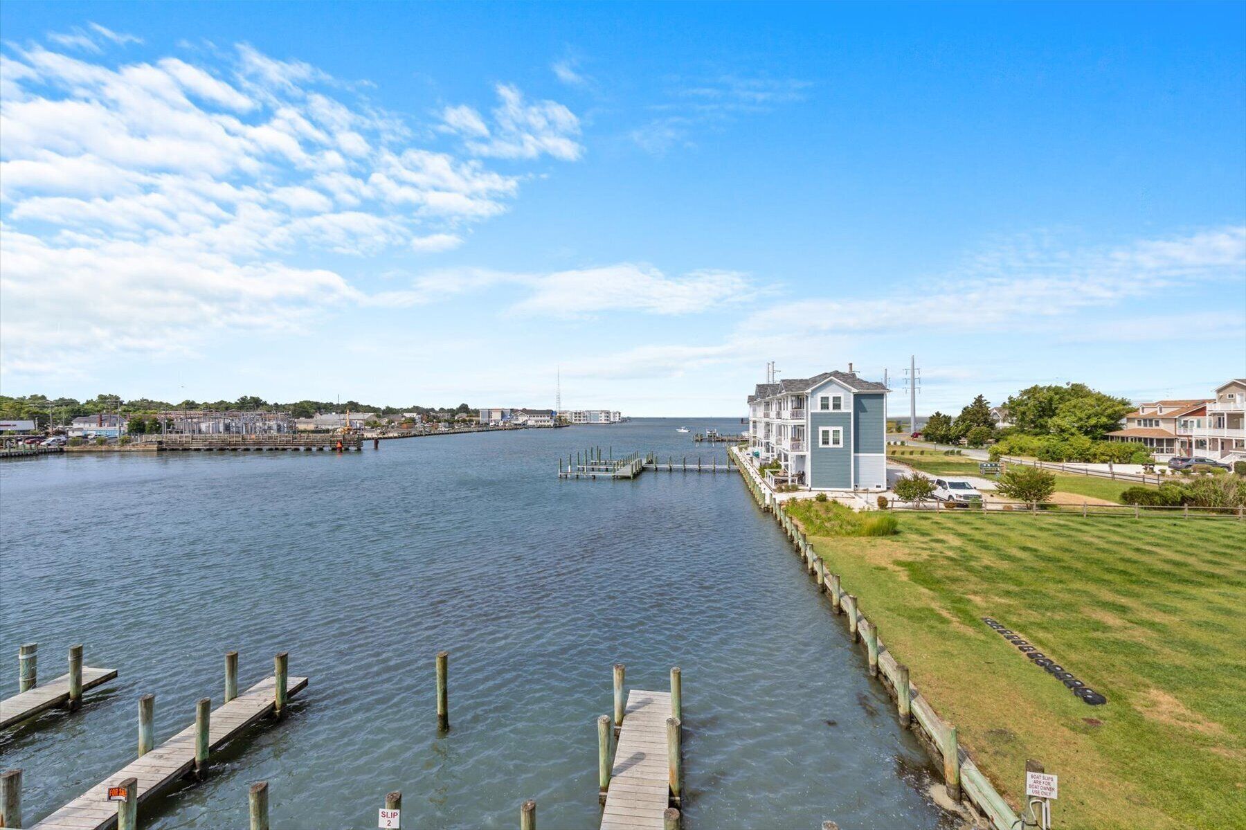 A waterfront property with a dock, a large house with a balcony, and a grassy area.