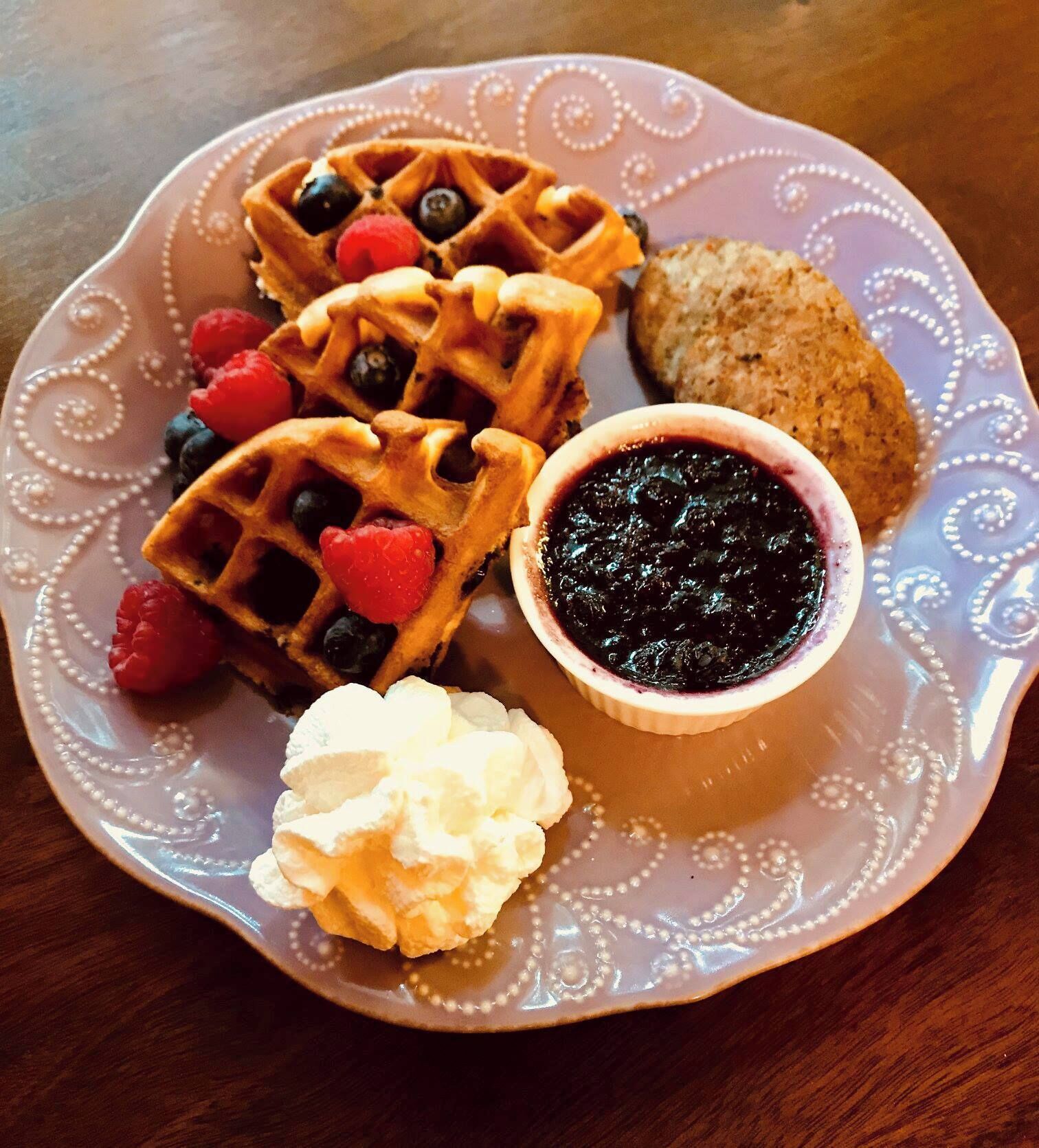 Un plato con waffles, frutos rojos, un bizcocho y un bol de mermelada.