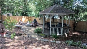 Un pabellón con terraza de madera, rodeado por una valla también de madera, y un área de patio con mobiliario exterior.
