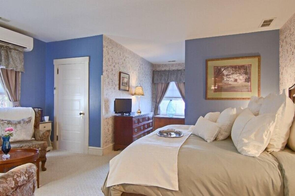 Een slaapkamer met een bed, een dressoir, een televisie en een raam met gordijnen.