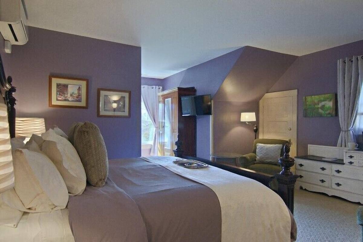 Een slaapkamer met een groot bed, een dressoir, een televisie en ingelijste foto’s aan de muur.