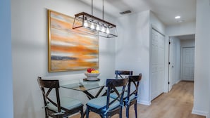 Un comedor moderno con una mesa de vidrio, cuatro sillas y una lámpara colgante.