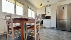 Une cuisine moderne avec des meubles blancs, un réfrigérateur en acier inoxydable et une table à manger avec des chaises.