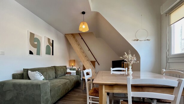 Un espace de vie moderne avec un canapé vert, des chaises blanches, une table à manger en bois et un plafond en pente avec des poutres apparentes.