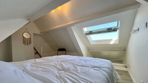 Une chambre avec un plafond en pente, un puits de lumière, un lit et une petite chaise.