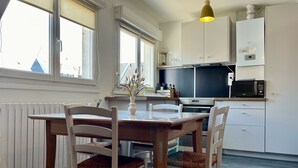Une cuisine avec des meubles blancs, une table à manger avec des chaises, un four à micro-ondes et un luminaire suspendu.