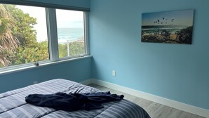 Un dormitorio con un ventanal grande, una cama con colcha a rayas y un cuadro de pájaros en la pared.