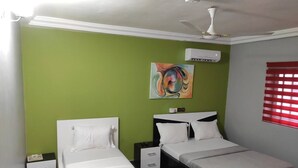 Un dormitorio con dos camas, ventilador de techo, equipo de aire acondicionado y ventana con persianas.
