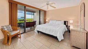 A hotel room with a bed, a chair, a nightstand, a ceiling fan, and a sliding glass door leading to an outdoor area.