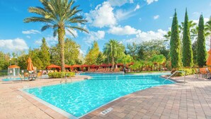 A swimming pool with a tiled deck, surrounded by palm trees and red-roofed structures. - Splendid Renovated 2 + 2 Condo Near Disney with Amazing Amenities (Davenport)