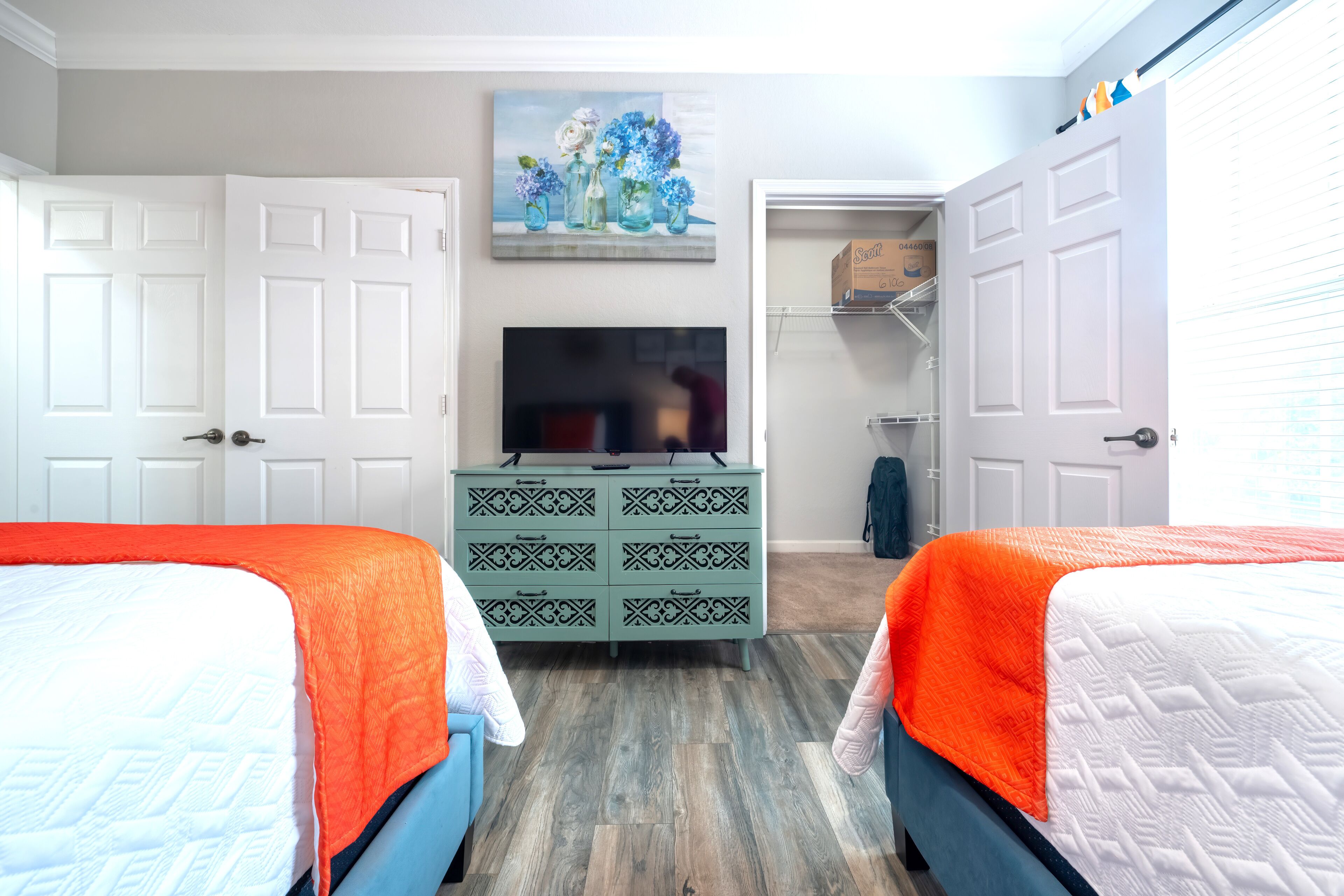 A bedroom with two beds, a dresser, a television, and a closet.