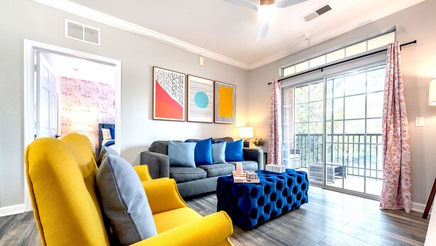 A modern living room with a sofa, armchair, ottoman, and a large window with curtains. - Splendid Renovated 2 + 2 Condo Near Disney with Amazing Amenities (Davenport)