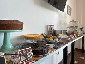 A buffet counter with various desserts and bread, a television mounted on the wall, and a tiled floor.