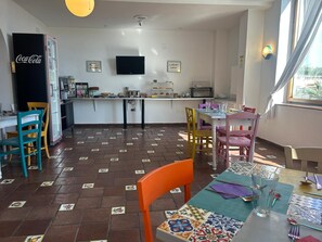 A restaurant with a tiled floor, a Coca-Cola refrigerator, a TV mounted on the wall, and a window with curtains.