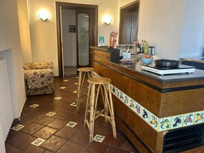 Une cuisine avec un coin bar, des tabourets, une cuisinière et un sol carrelé.