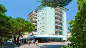 A multi-story hotel with a light blue facade, balconies on each floor, and a blue awning over the entrance. - Spacious Flat With sea View Terrace - Beahost (San Michele al Tagliamento)