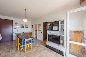 A dining area with a table and chairs, a television, and a bookshelf. - Spacious Flat With sea View Terrace - Beahost (San Michele al Tagliamento)