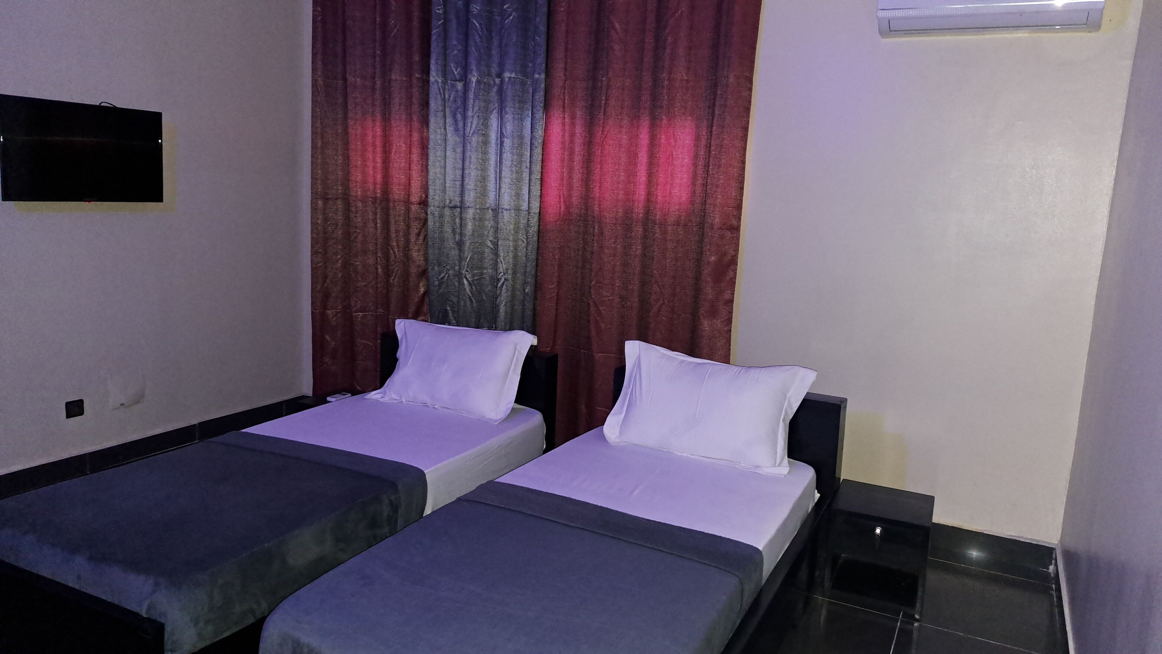 A room with two single beds, a small TV on the wall, and a window with curtains.