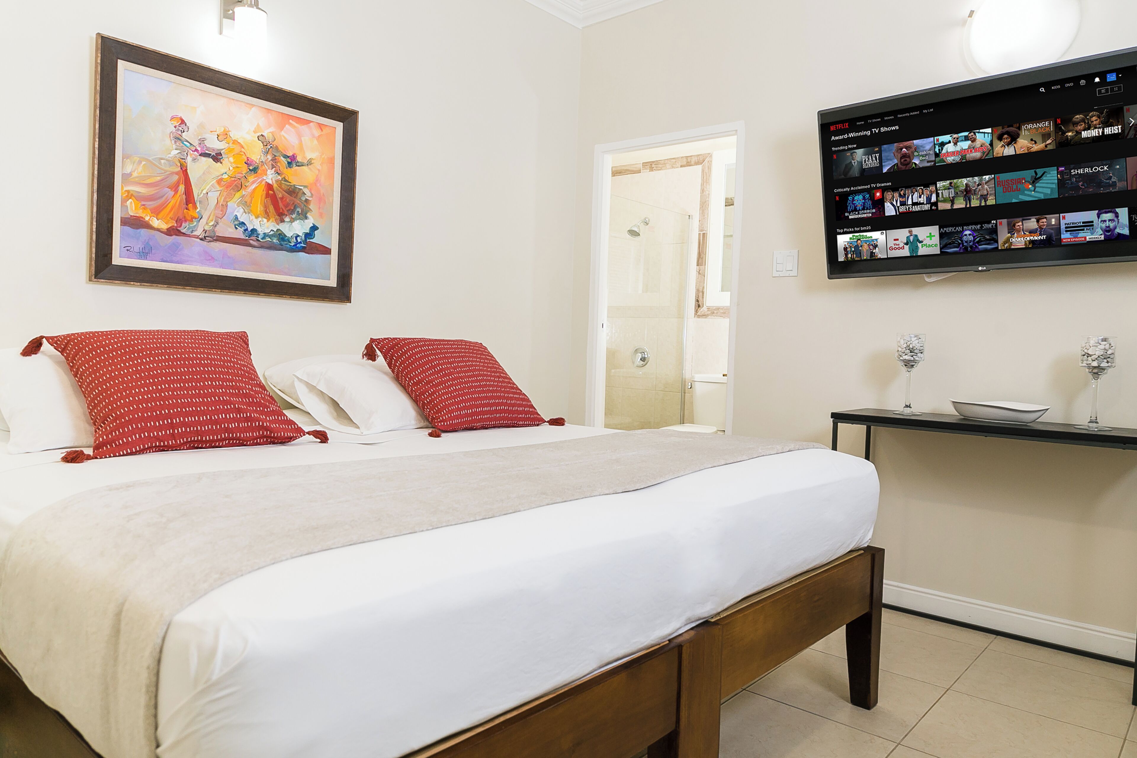Une chambre d’hôtel avec un lit, un téléviseur fixé au mur et un tableau au-dessus du lit.