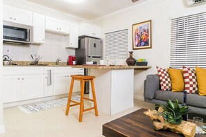 A modern kitchen with white cabinets, stainless steel appliances, a wooden stool, and a grey sofa with checkered cushions. - Charming Studio With Garden Oasis in Kingston (Kingston)
